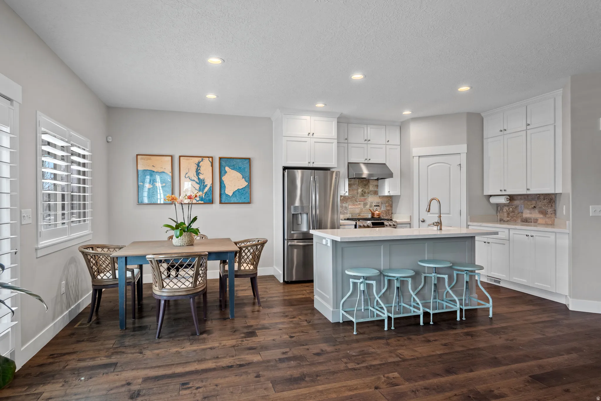 Kitchen with a breakfast bar area, stainless steel fridge, white cabinets, recessed lighting, and a kitchen island with sink