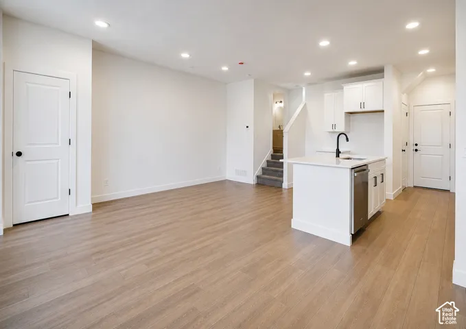Open-concept living space with wood-finish flooring, recessed lighting, white cabinetry, a kitchen island with sink, and a stainless steel dishwasher