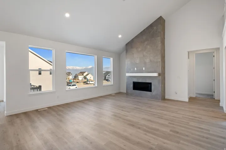 Unfurnished living room featuring lofted ceiling, light wood finished floors, a fireplace, plenty of natural light, and recessed lighting