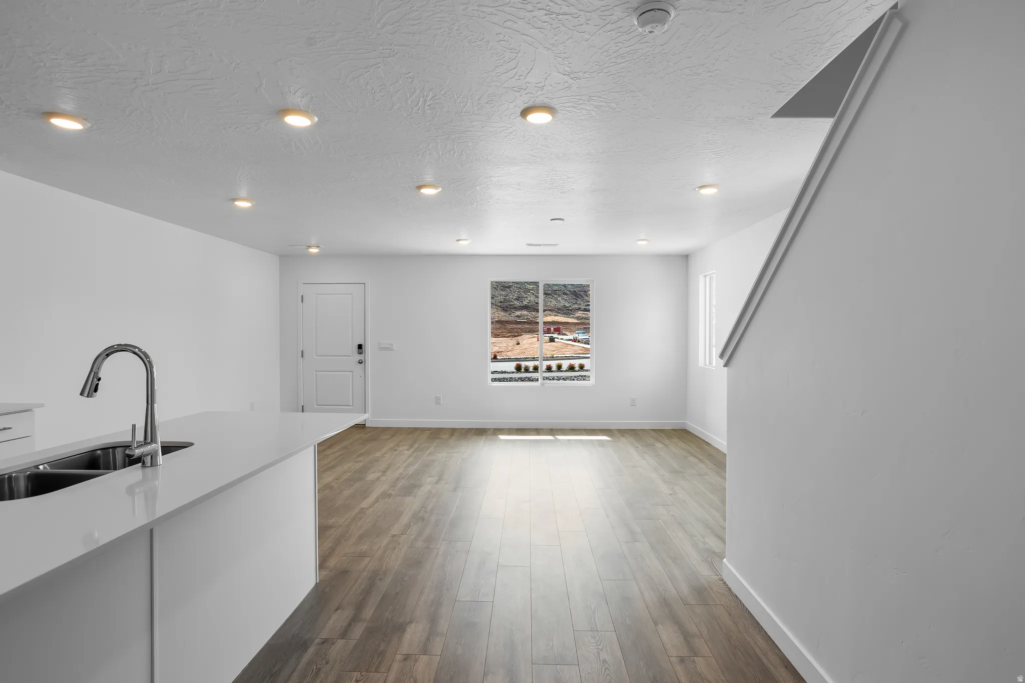 Kitchen featuring dark wood-type flooring, light stone counters, a textured ceiling, open floor plan, and white cabinets