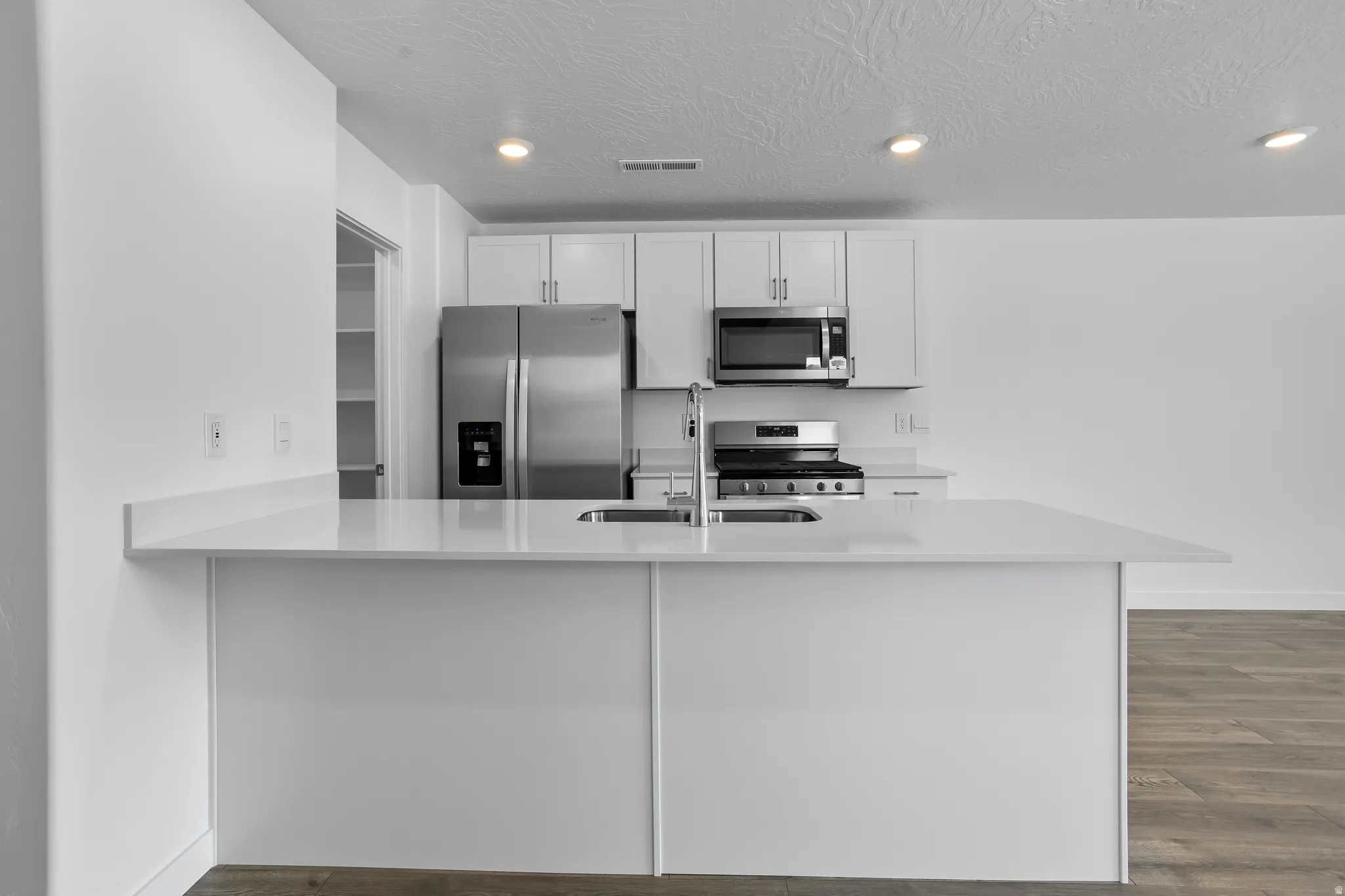 Kitchen featuring stainless steel appliances, dark wood finished floors, a peninsula, white cabinets, and light stone counters