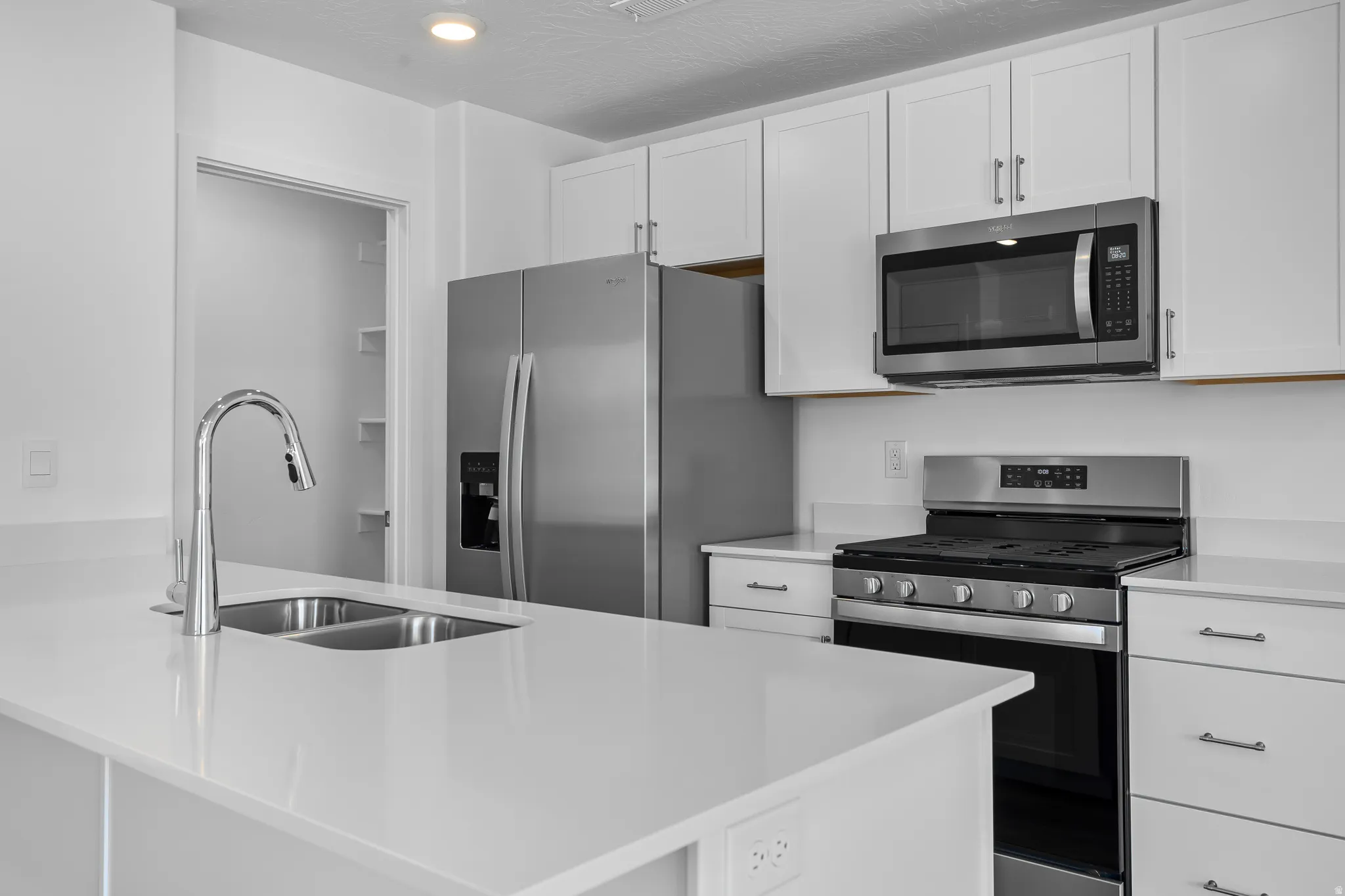 Kitchen featuring stainless steel appliances, a peninsula, white cabinetry, and light stone countertops