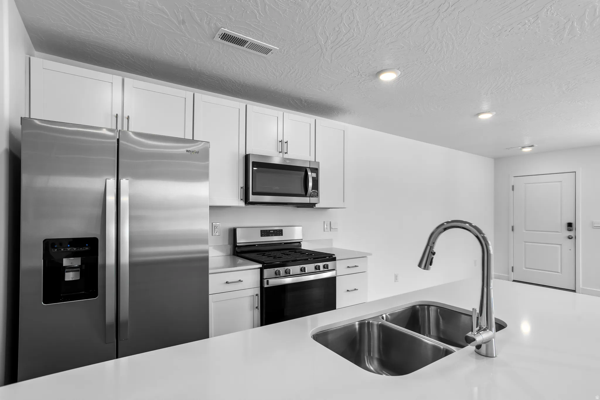Kitchen with stainless steel appliances, white cabinets, and a textured ceiling