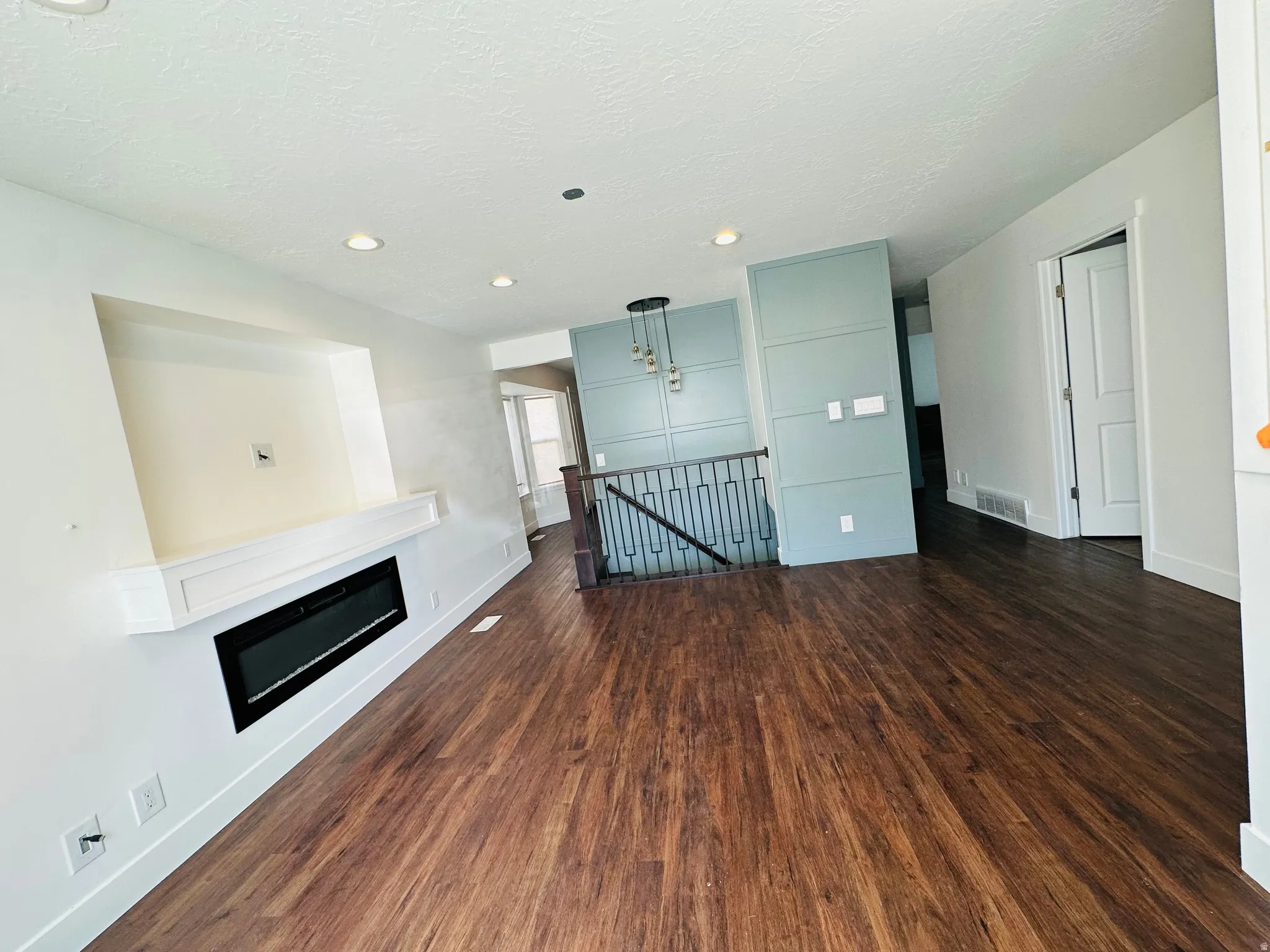 Unfurnished living room with dark wood-style flooring, a textured ceiling, a glass covered fireplace, and recessed lighting