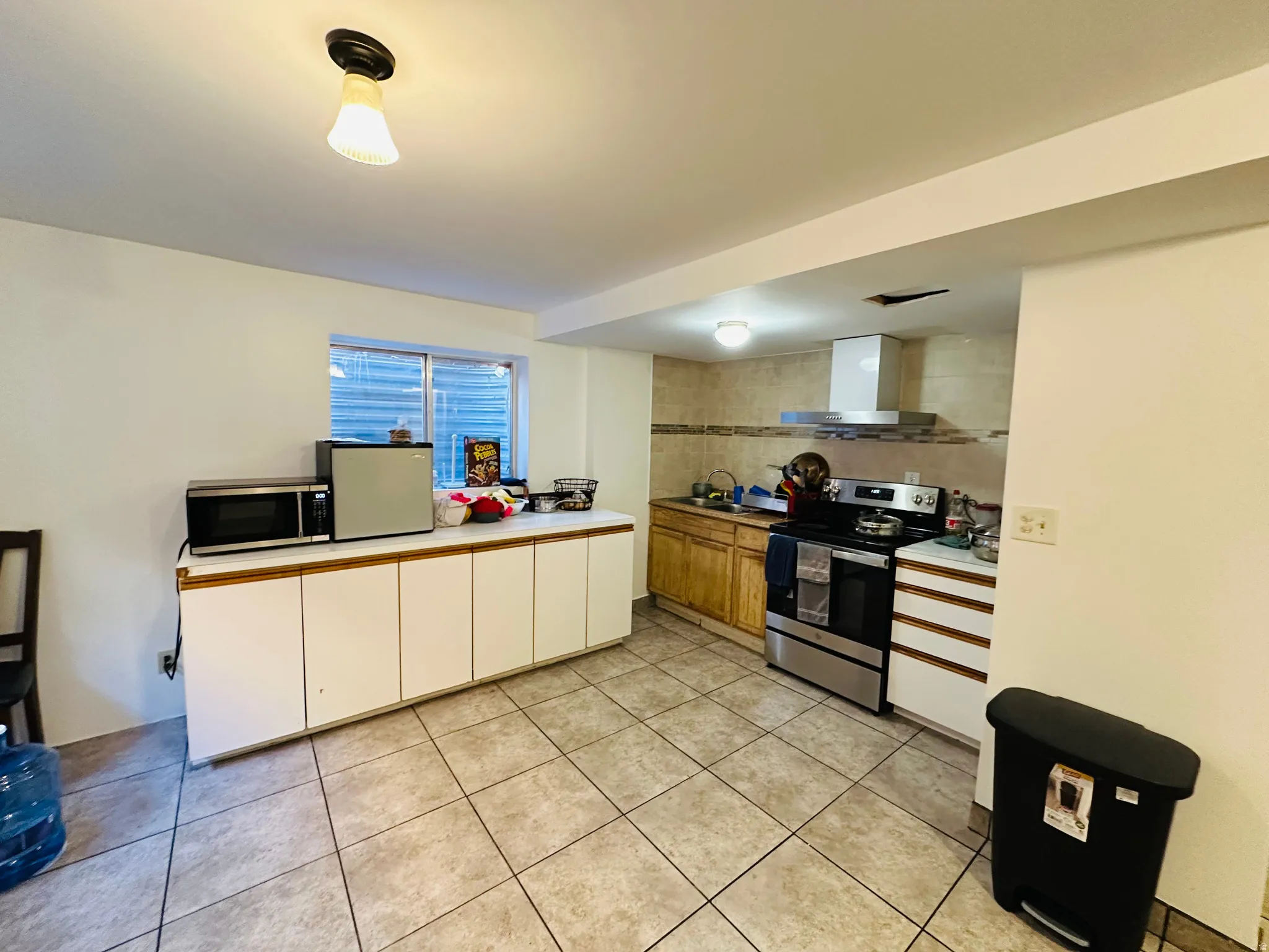 Kitchen featuring stainless steel appliances, light tile patterned floors, light countertops, white cabinetry, and wood finish cabinets