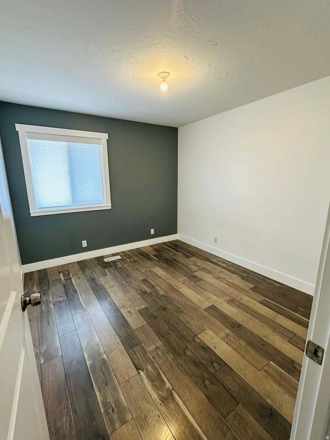 Unfurnished room featuring dark wood-style flooring and a textured ceiling