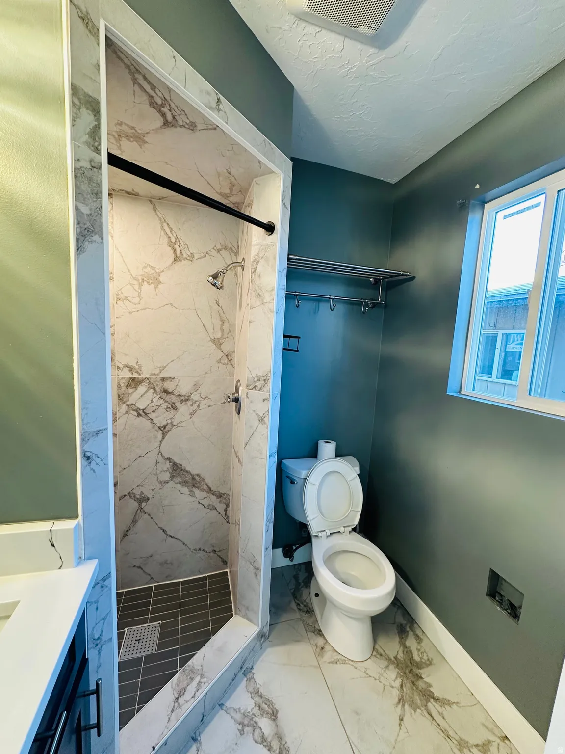 Bathroom featuring a marble finish shower, vanity, marble look tile flooring, and a textured ceiling