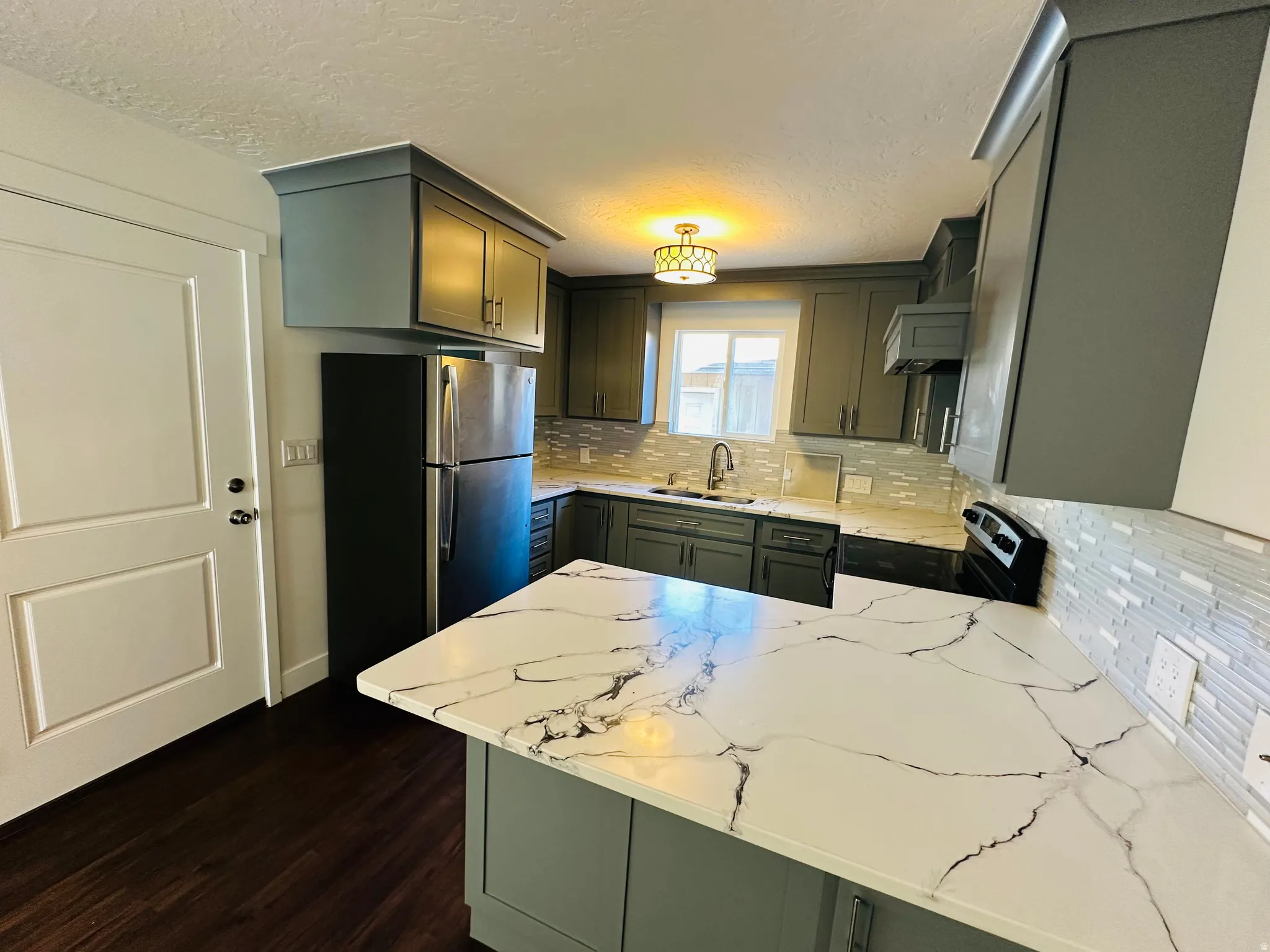 Kitchen with tasteful backsplash, a peninsula, freestanding refrigerator, light stone counters, and dark wood-type flooring