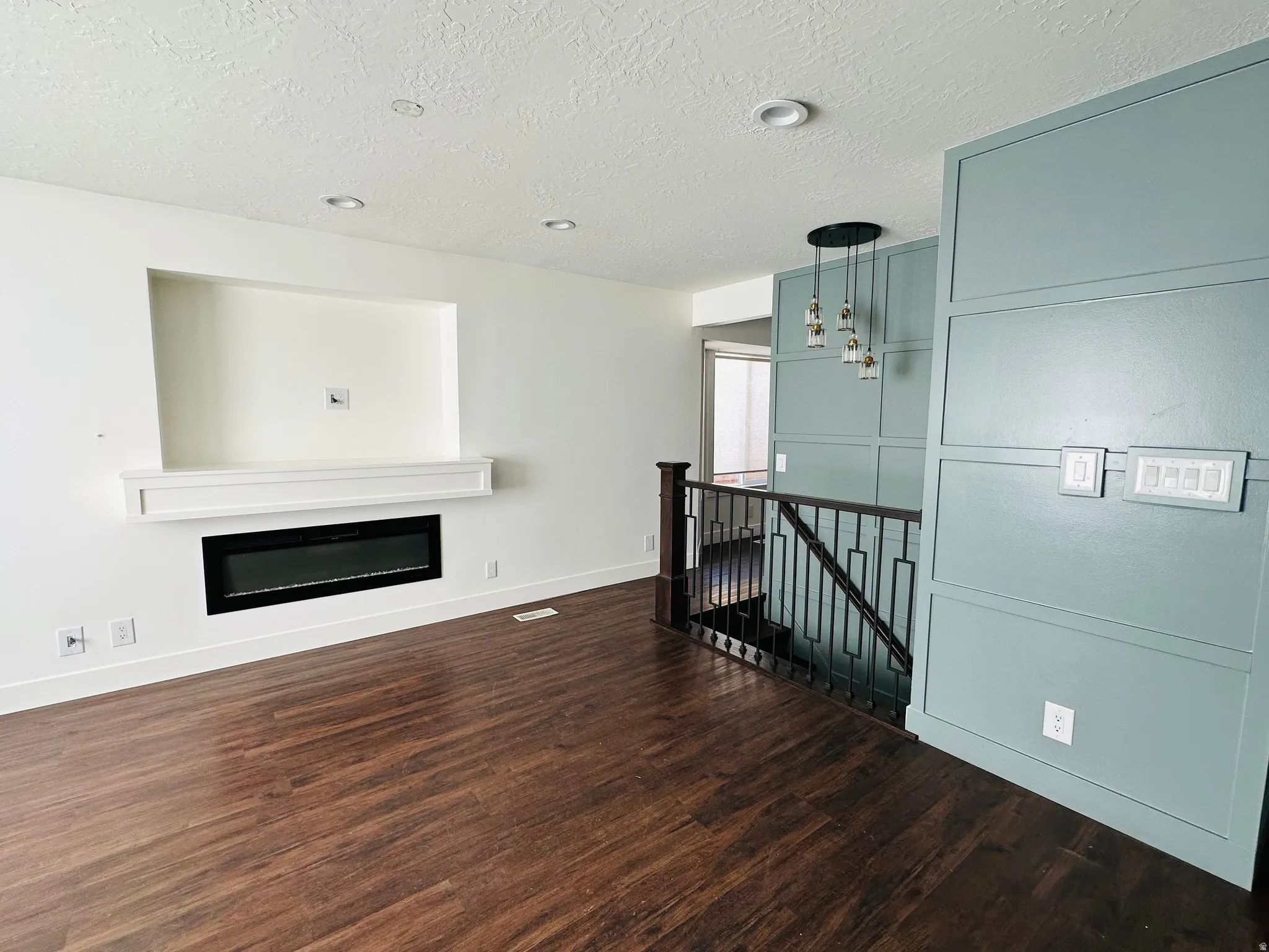Unfurnished living room with dark wood-type flooring, a glass covered fireplace, a textured ceiling, and suspended lighting