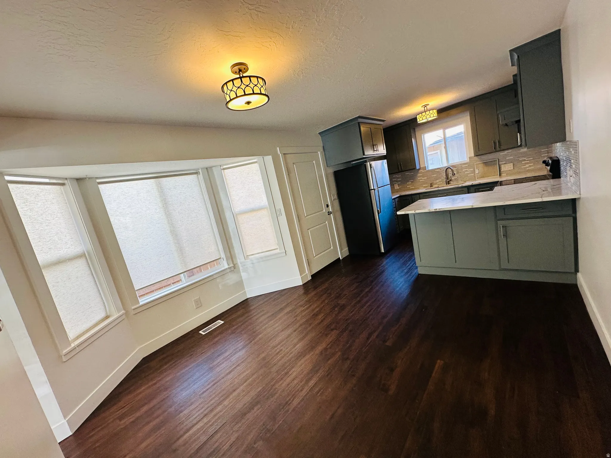 Kitchen featuring a peninsula, freestanding refrigerator, dark wood-style flooring, tasteful backsplash, and a textured ceiling