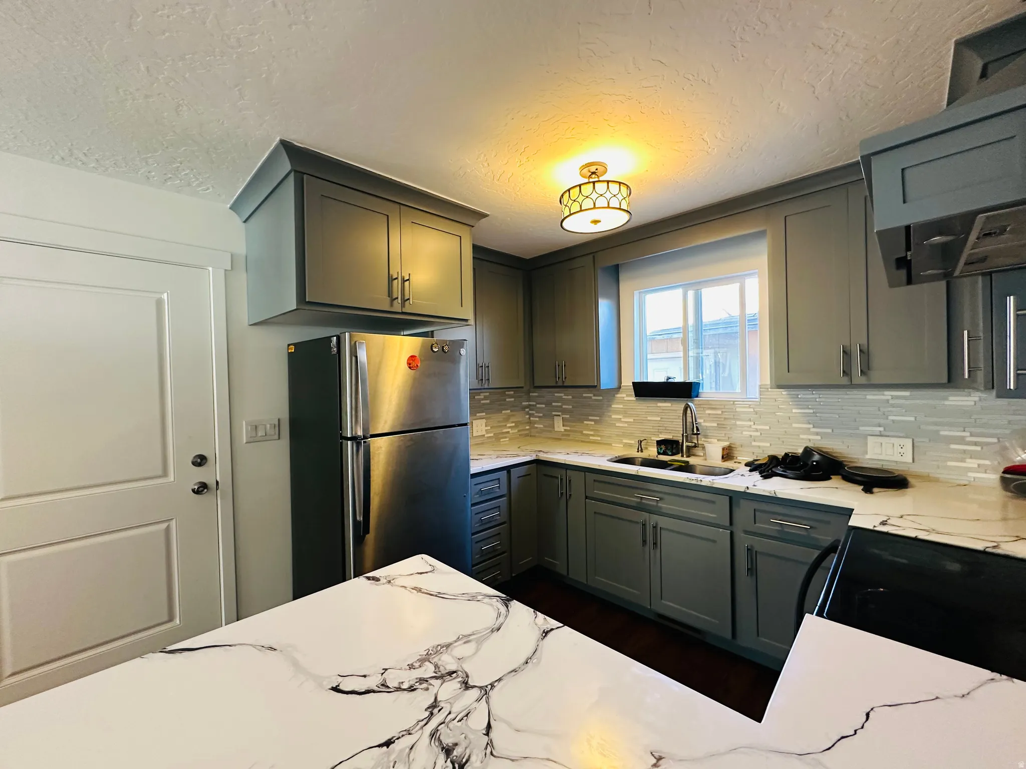 Kitchen featuring freestanding refrigerator, a textured ceiling, black electric range, gray cabinetry, and light stone counters
