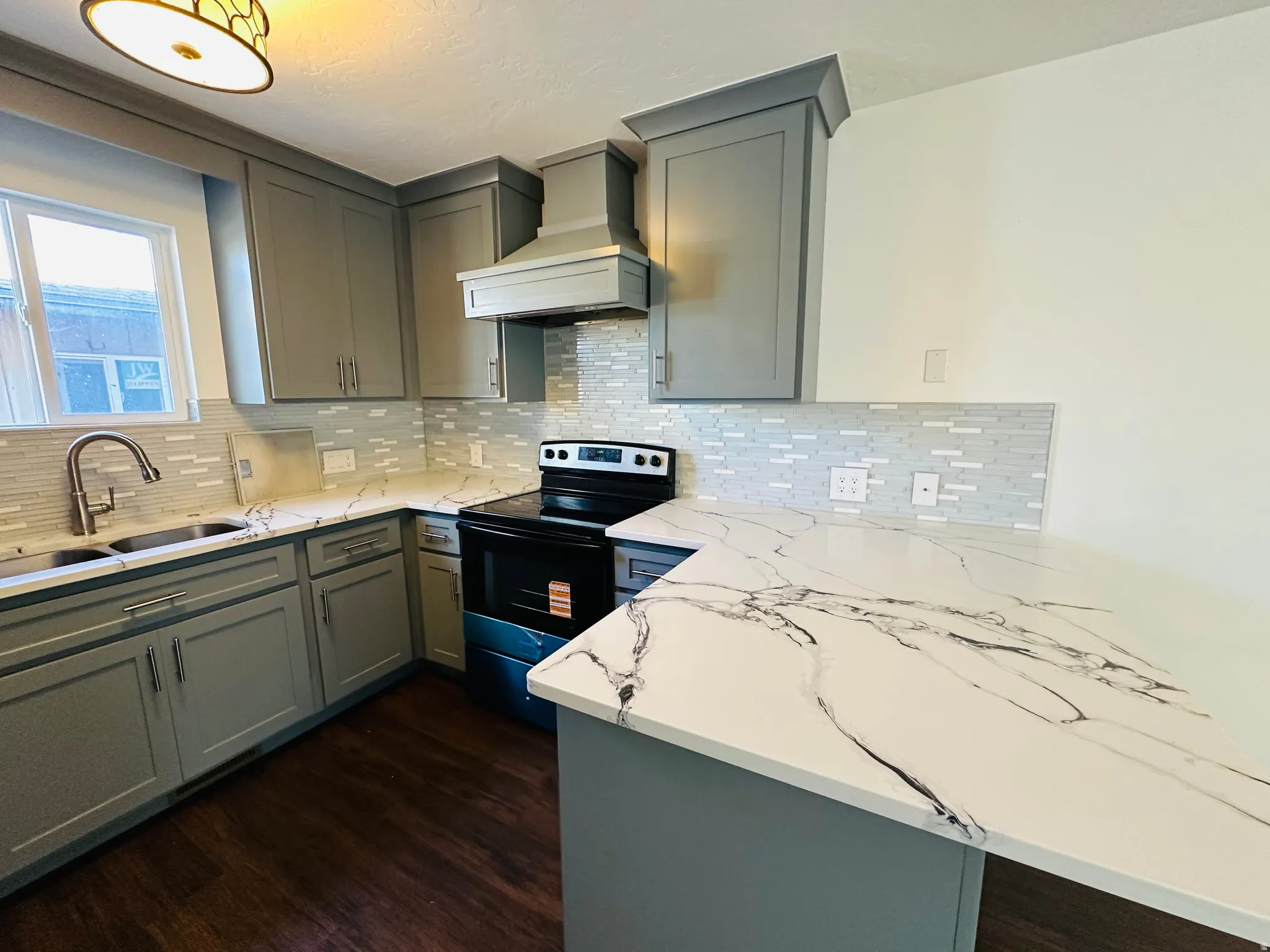 Kitchen with range with electric cooktop, gray cabinetry, light stone counters, a peninsula, and dark wood-style floors