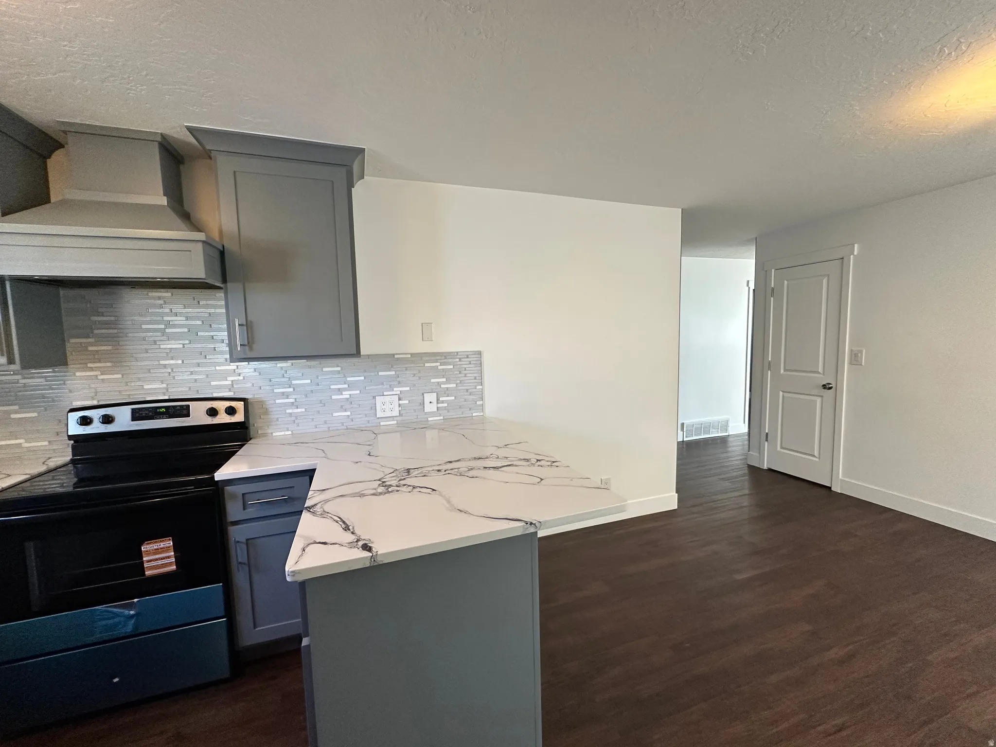 Kitchen with stainless steel electric range, gray cabinets, a textured ceiling, a peninsula, and dark wood-style floors