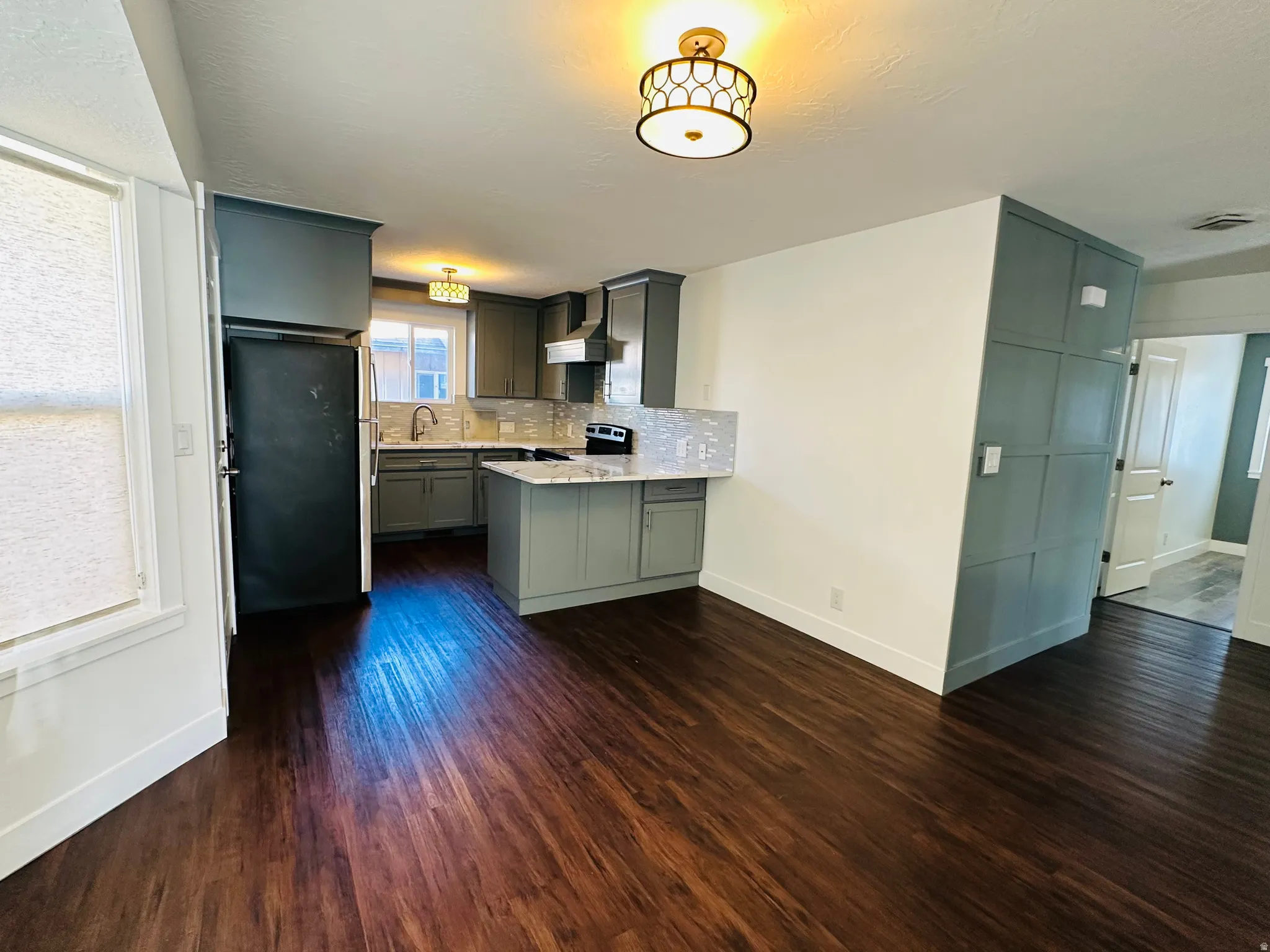 Kitchen with tasteful backsplash, stainless steel appliances, dark wood-style flooring, gray cabinets, and a peninsula