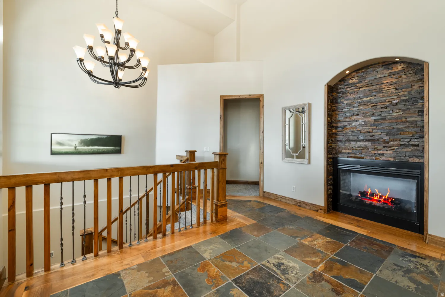 Corridor featuring an upstairs landing, stone tile flooring, a high ceiling, and hanging lights