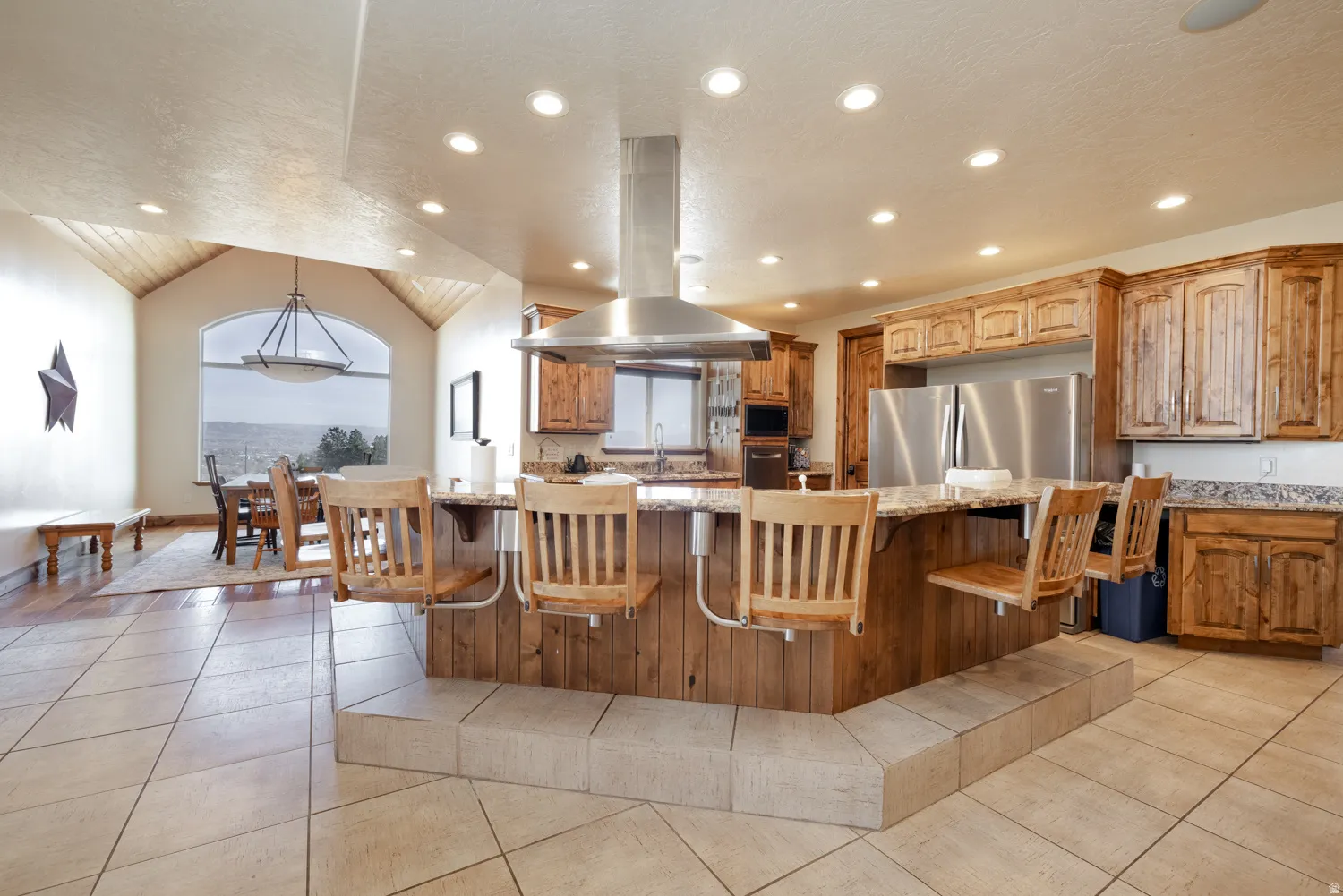 Kitchen featuring island exhaust hood, light stone countertops, a breakfast bar, light tile patterned floors, and stainless steel appliances