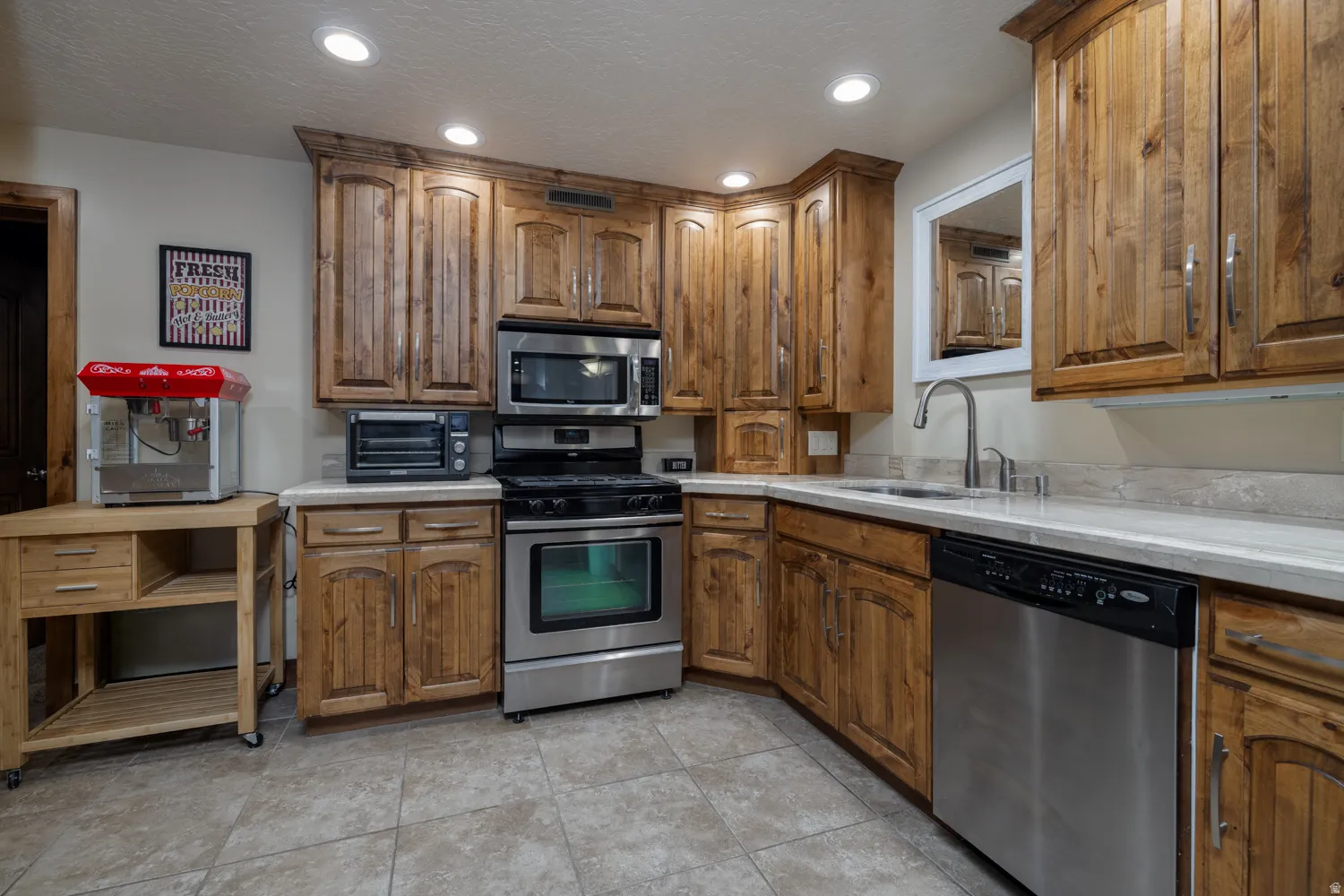 Kitchen with stainless steel appliances, wood finish cabinetry, recessed lighting, light countertops, and a textured ceiling
