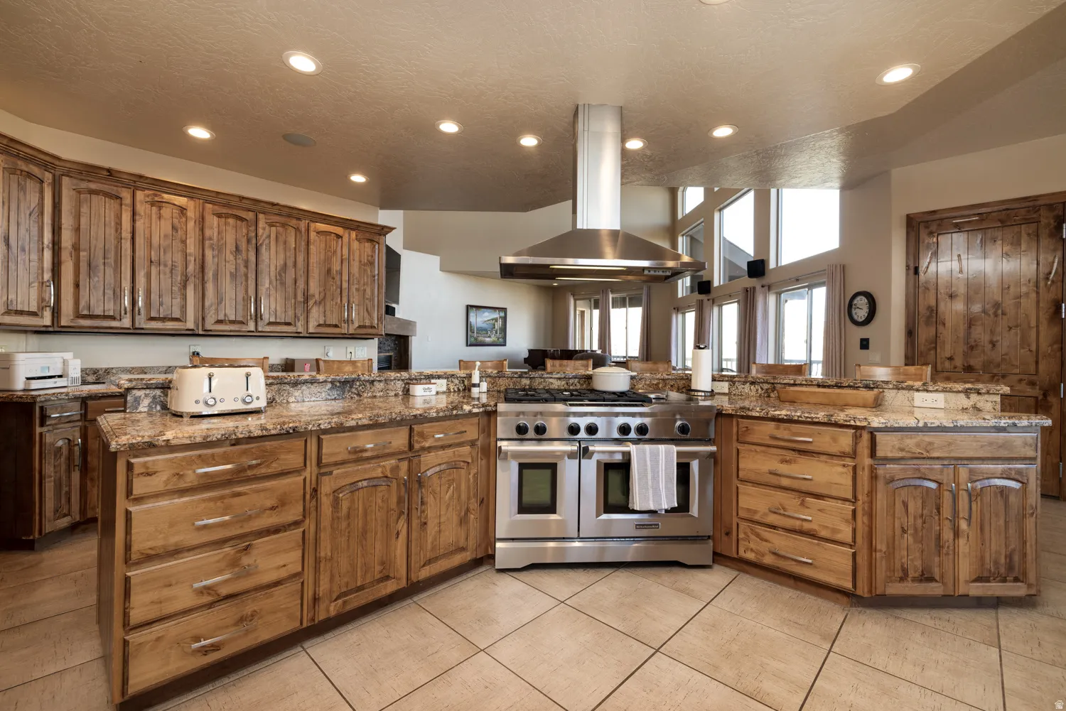 Kitchen with double oven range, island exhaust hood, dark stone countertops, recessed lighting, and wood finish cabinetry