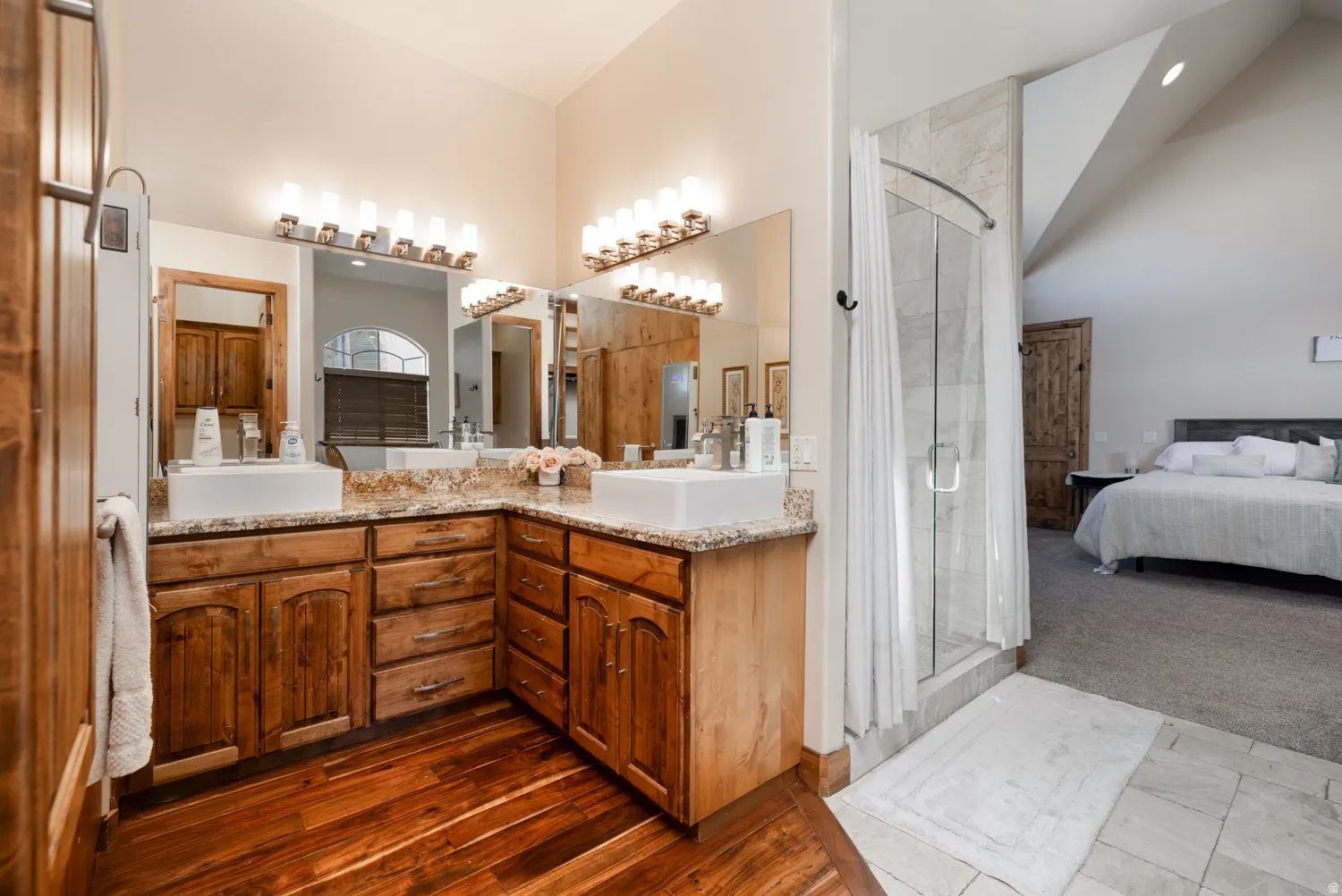 Ensuite bathroom featuring a stall shower, double vanity, dark carpet, and lofted ceiling