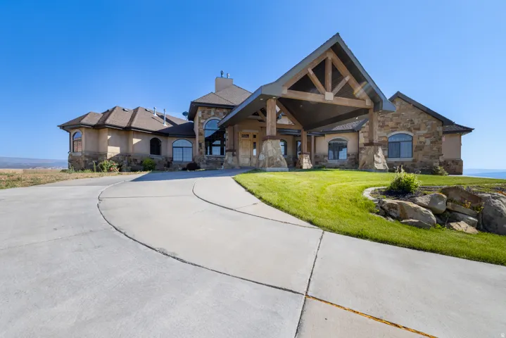 View of front of home with stone siding, a front yard, a chimney, and curved driveway