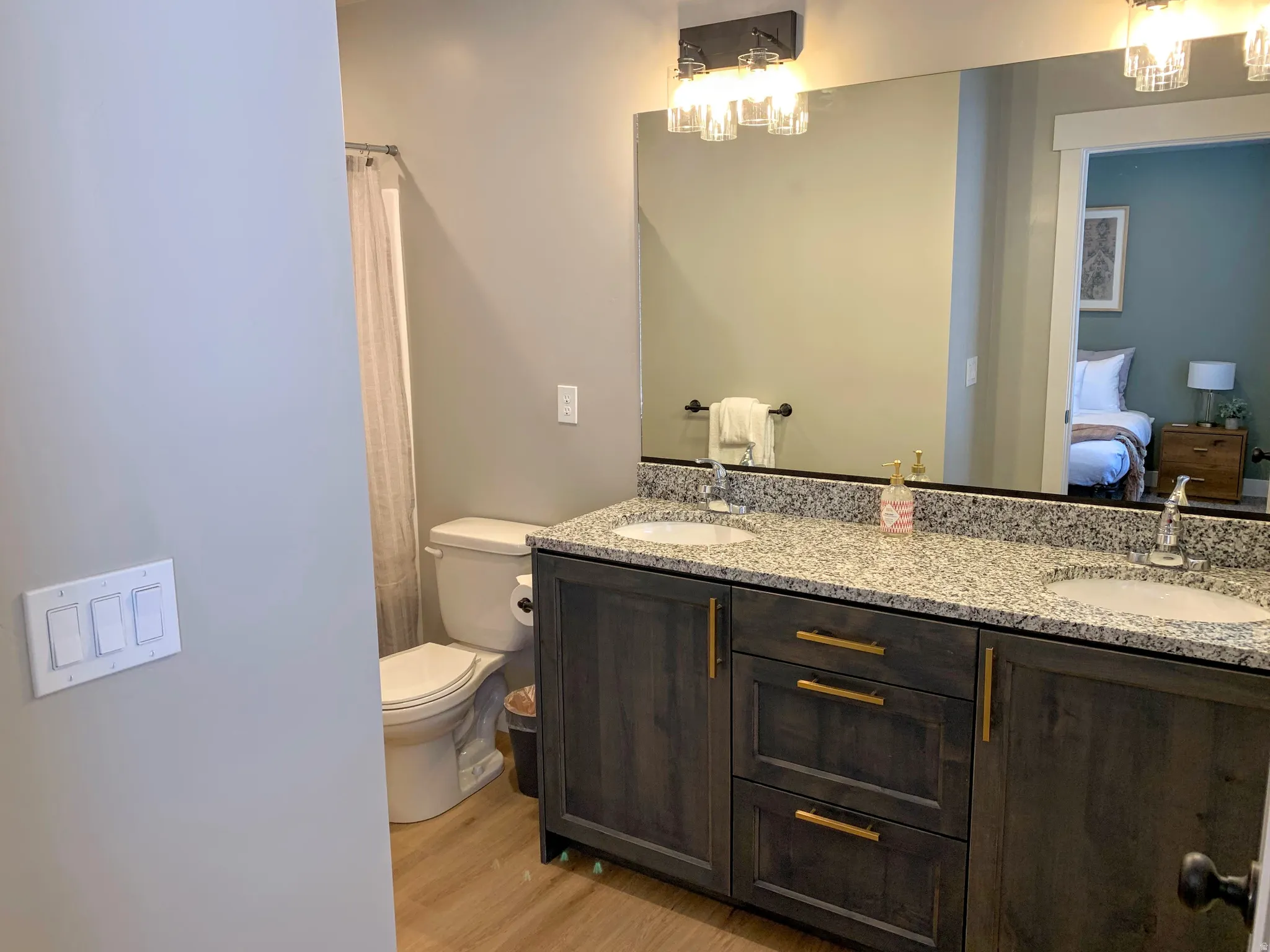 Ensuite bathroom featuring double vanity, light wood-type flooring, a shower with curtain, and hanging lights