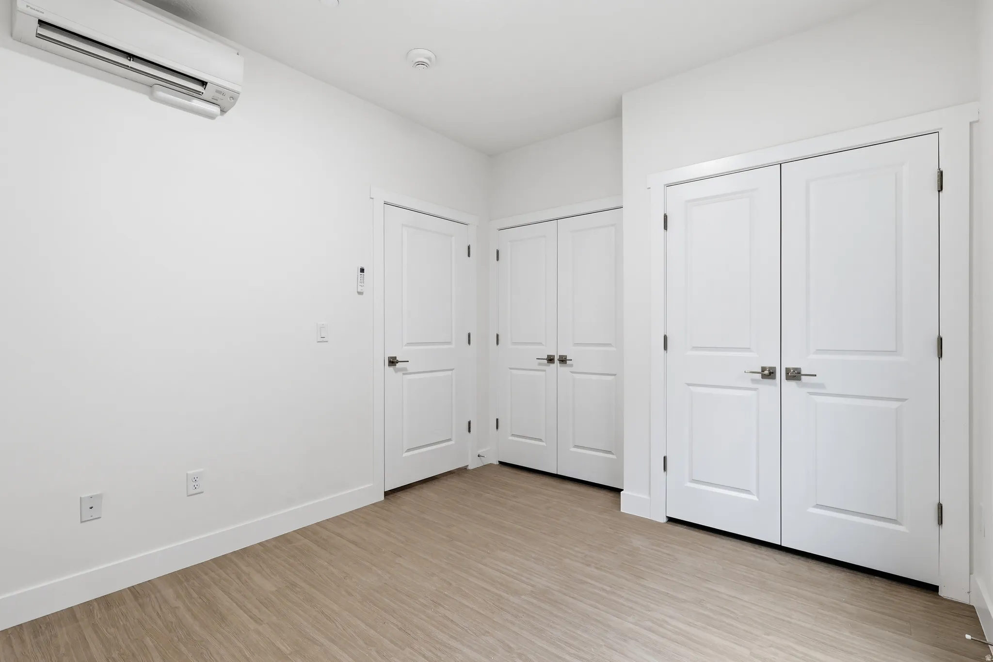 Bedroom featuring a wall mounted mini split, light wood-style flooring, and multiple closets