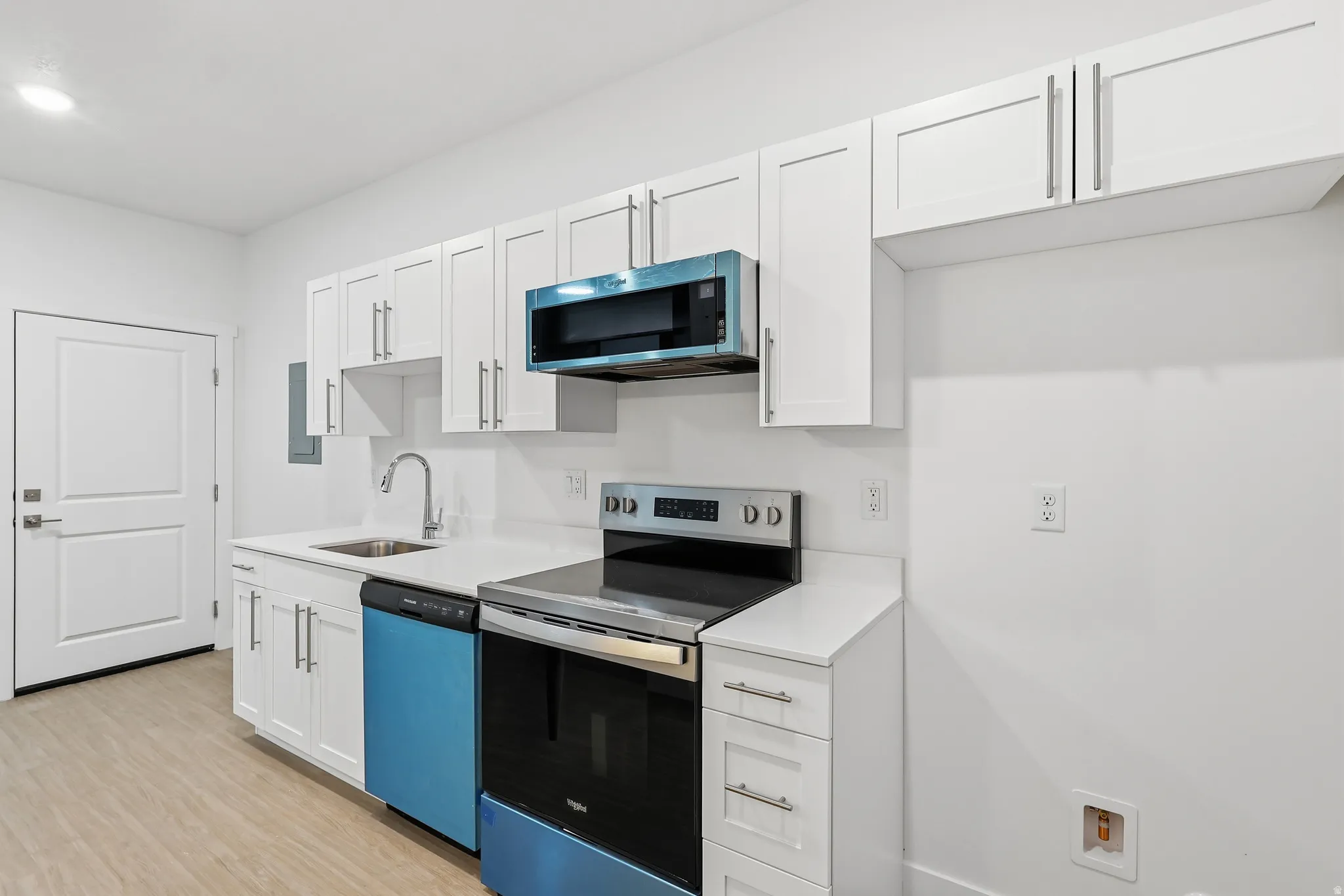 Kitchen with stainless steel appliances, white cabinets, and light wood-style floors