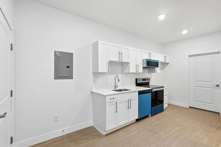 Entrance opens to with white cabinetry, range with electric stovetop, electric panel, light wood finished floors, and dishwashing machine