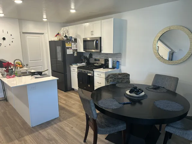 Kitchen featuring white cabinetry, stainless steel appliances, wood finished floors, tasteful backsplash, and a center island with sink