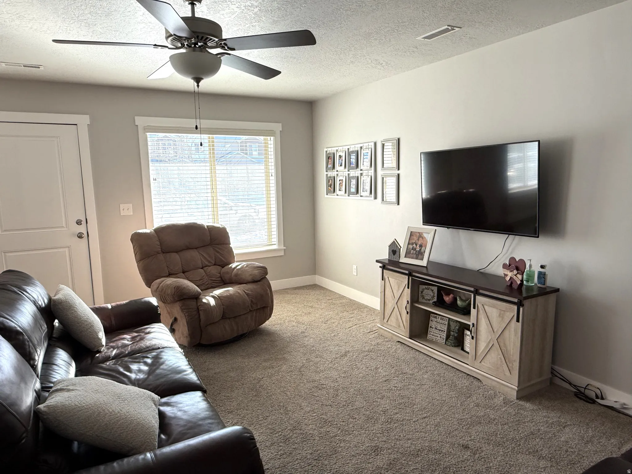 Living area with carpet, a ceiling fan, and a textured ceiling