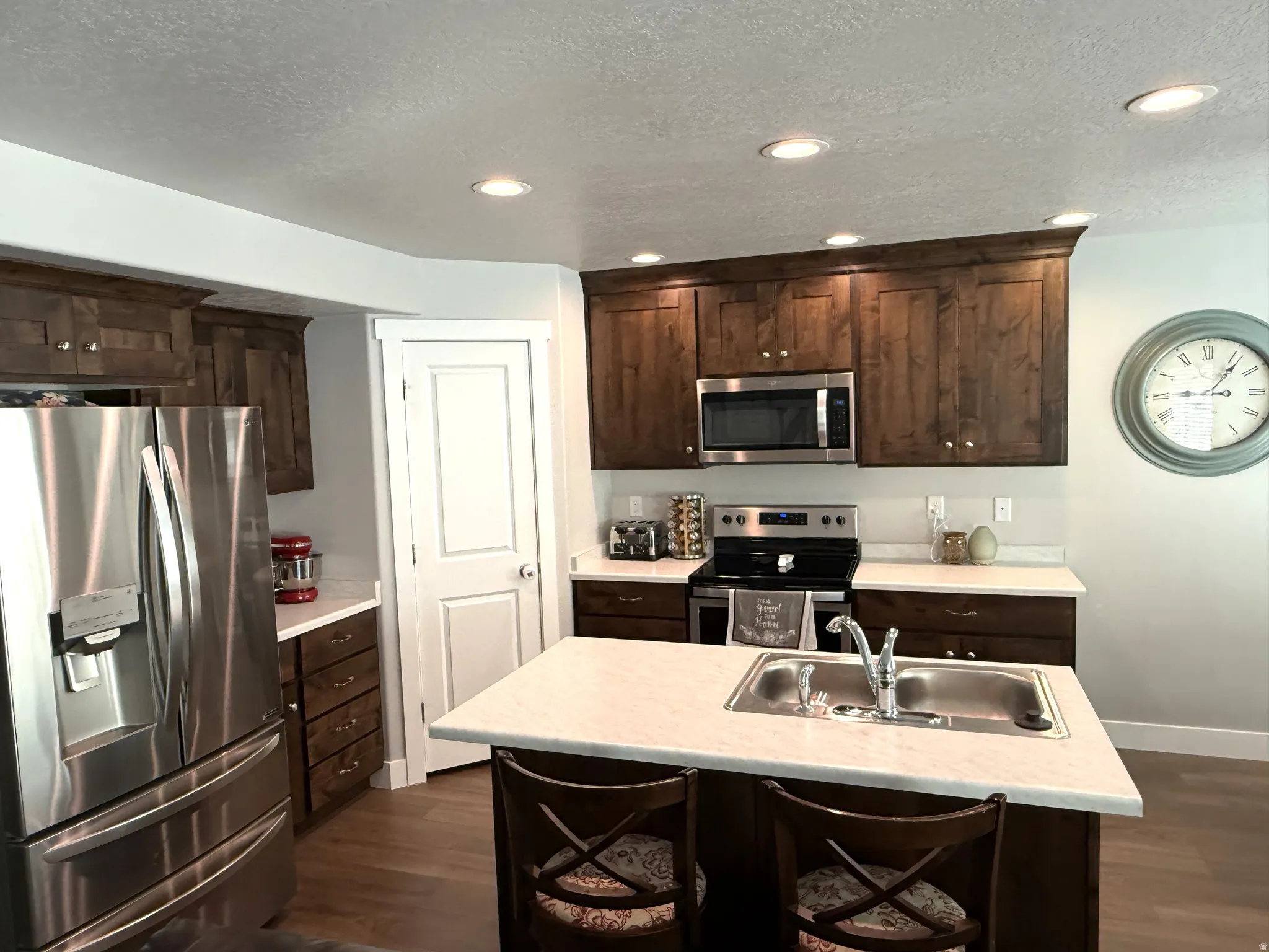 Kitchen featuring stainless steel appliances, dark wood finish cabinetry, light countertops, dark wood-style floors, and a textured ceiling