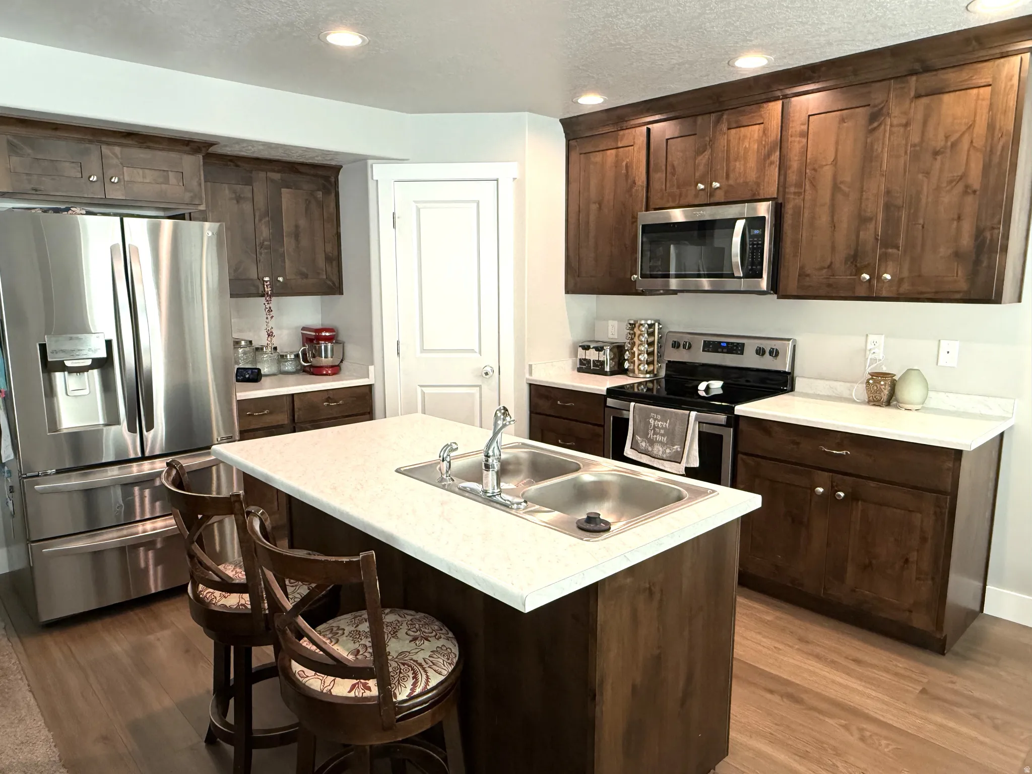 Kitchen featuring stainless steel appliances, light countertops, dark wood finish cabinetry, a kitchen island with sink, and a breakfast bar area