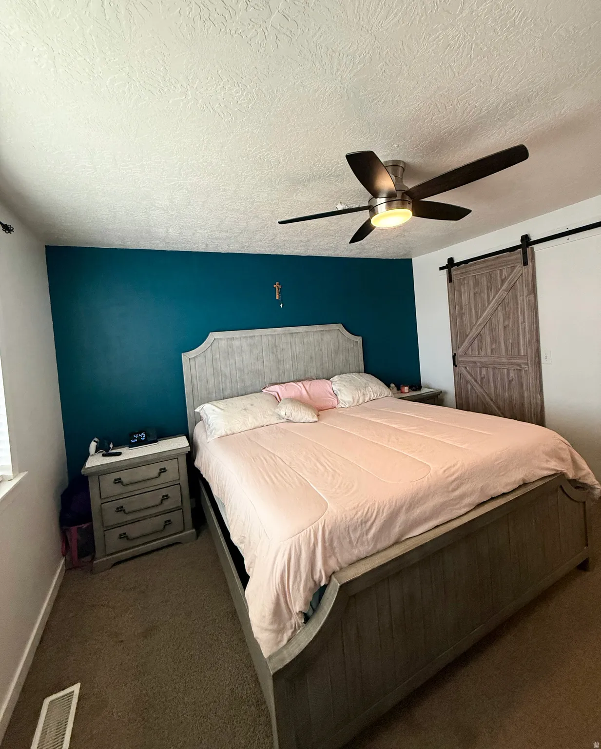 Carpeted bedroom featuring a barn door, a textured ceiling, and a ceiling fan