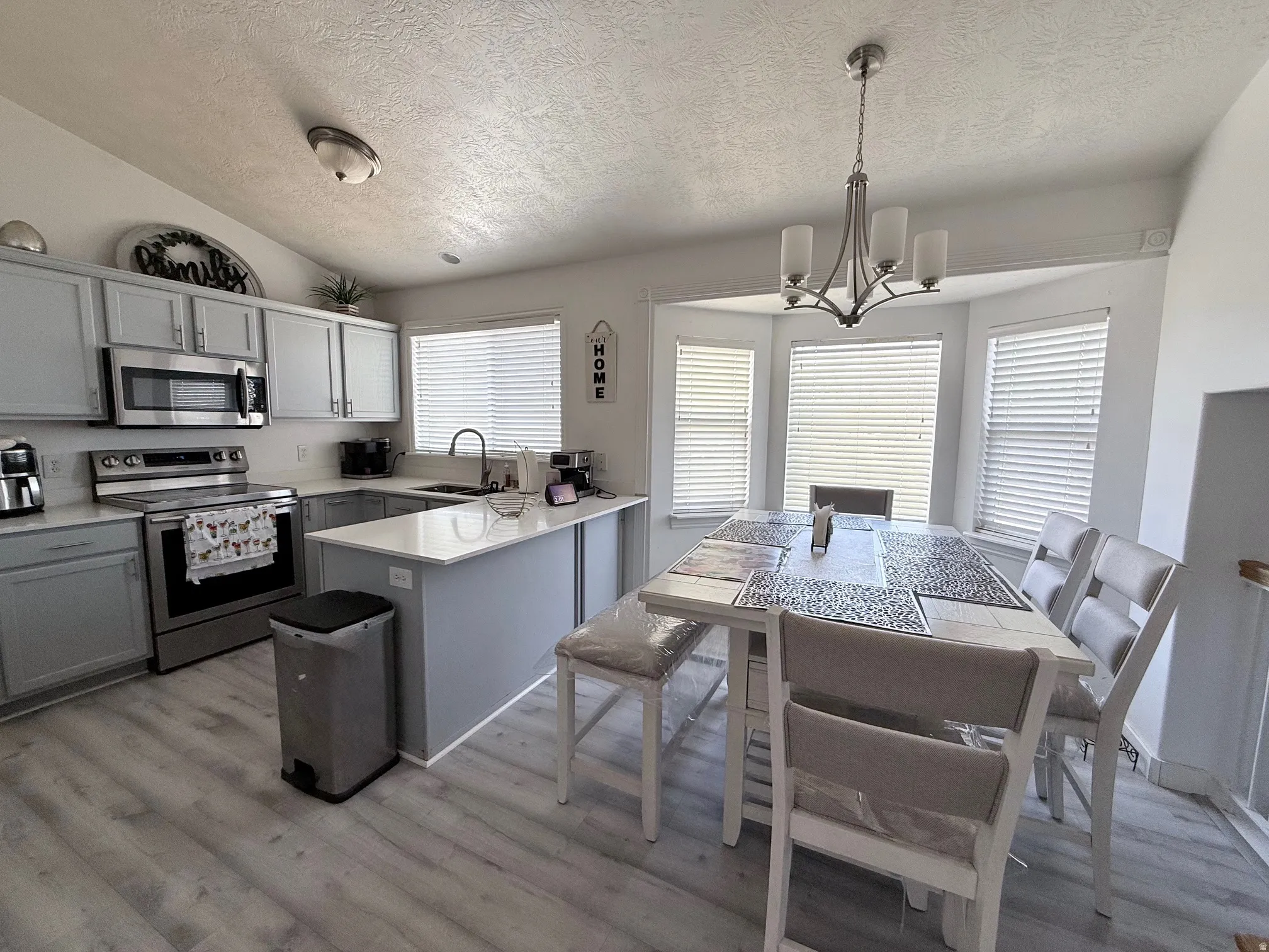 Kitchen featuring stainless steel appliances, light countertops, gray cabinets, a peninsula, and hanging lights