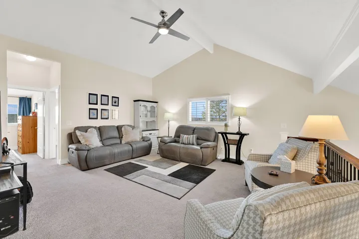 Carpeted living area with beamed ceiling, ceiling fan, and high vaulted ceiling