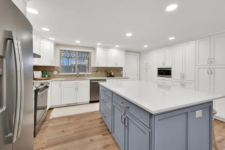 Kitchen featuring white cabinets, appliances with stainless steel finishes, light wood-type flooring, light stone counters, and gray cabinets
