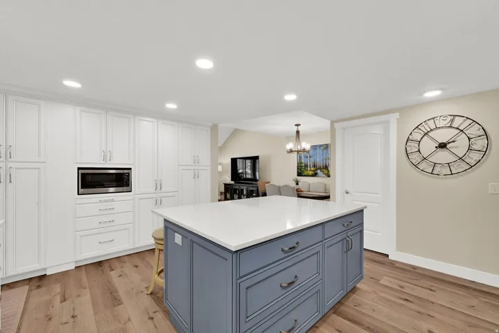 Kitchen with white cabinets, blue cabinets, a kitchen island, light stone countertops, and recessed lighting