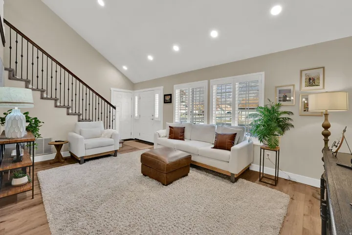 Living room with recessed lighting, high vaulted ceiling, light wood finished floors, and stairs