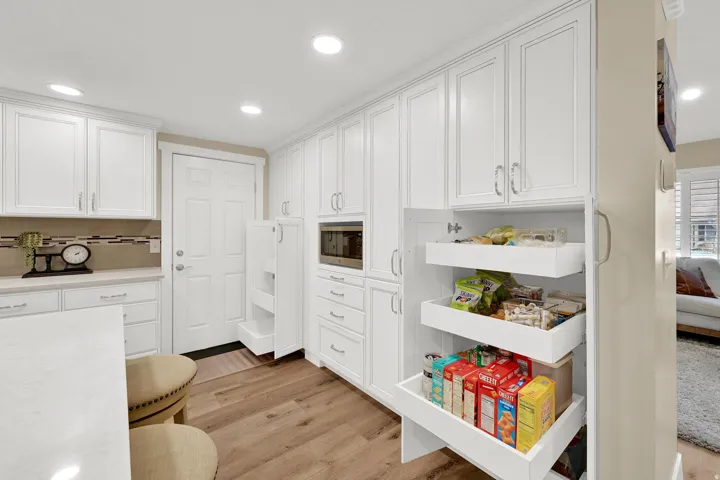 Kitchen with white cabinetry, light wood-style flooring, recessed lighting, stainless steel microwave, and tasteful backsplash