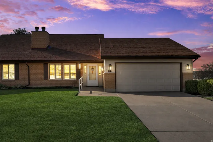 View of front facade featuring an attached garage, concrete driveway, a lawn, a chimney, and brick siding