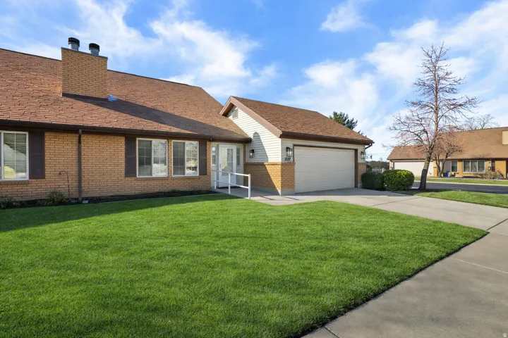 View of front of home with a front lawn, brick siding, driveway, a chimney, and an attached garage