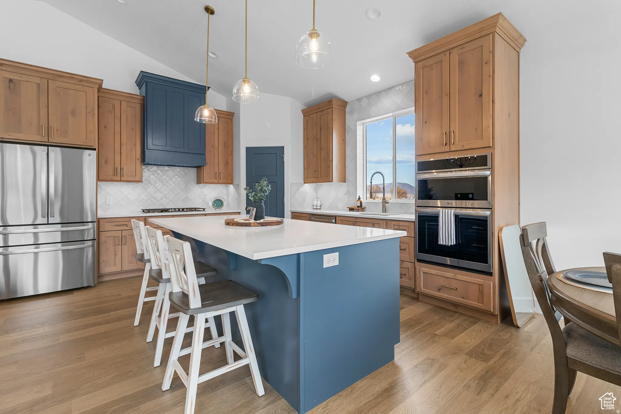 Dual tone kitchen with stainless steel appliances, a kitchen bar, a kitchen island, tasteful backsplash, and hanging light fixtures