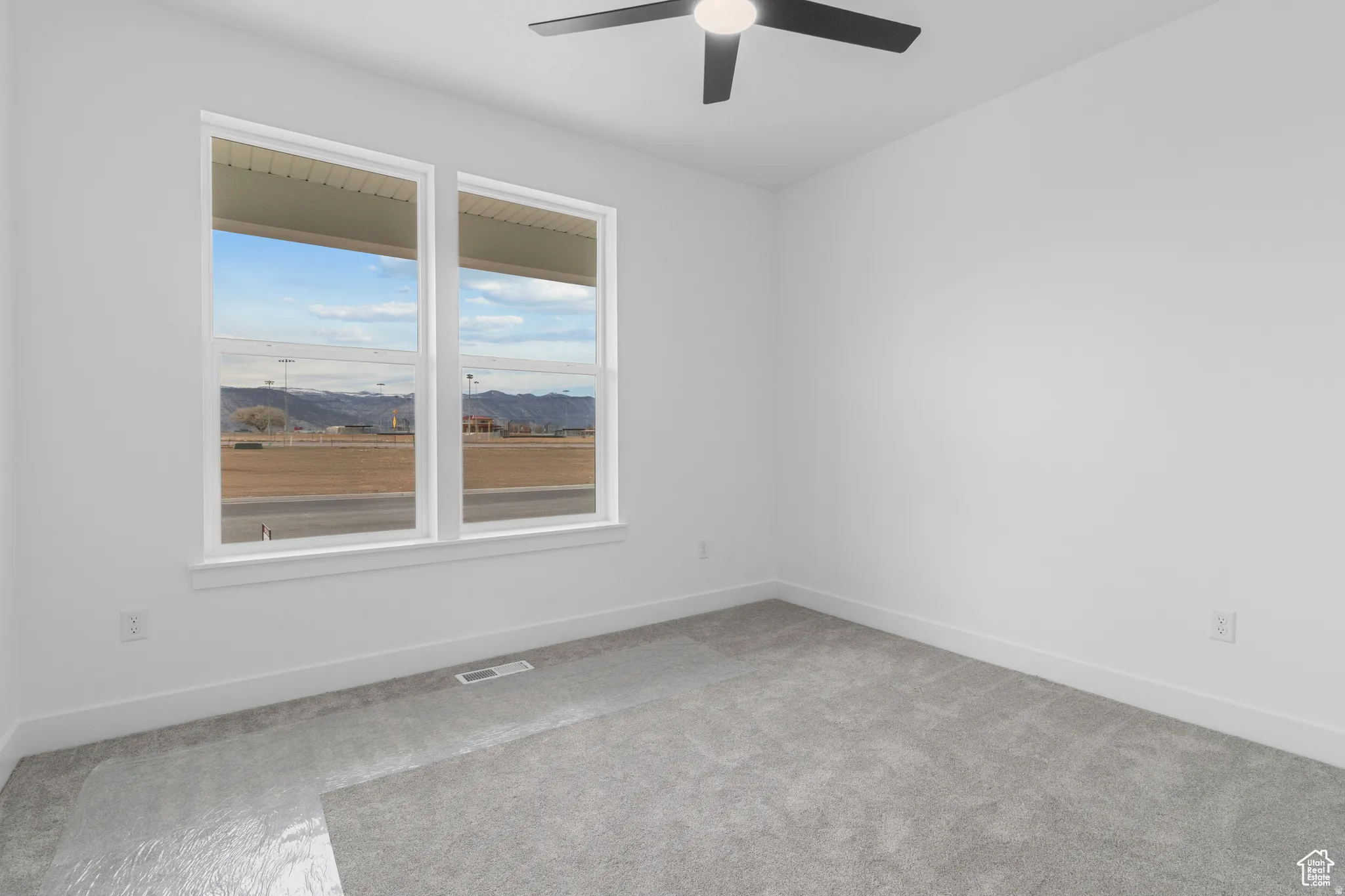 Empty room with a mountain view, light colored carpet, and a ceiling fan