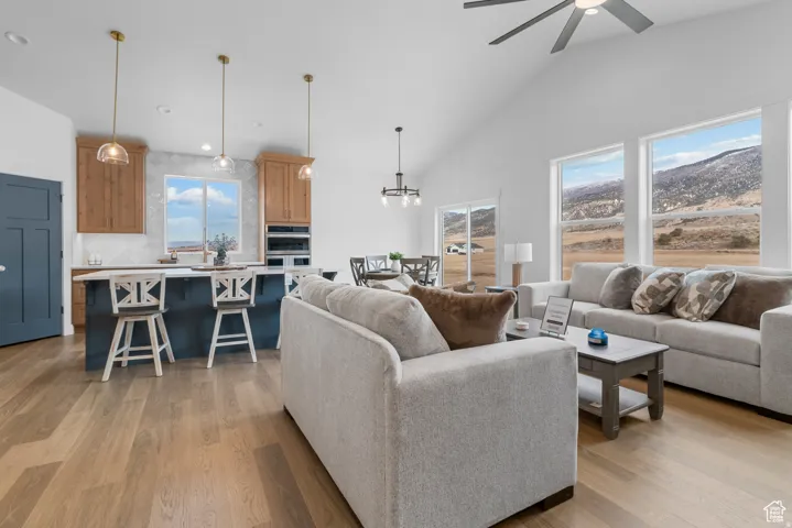 Living room with light wood-style flooring, vaulted ceiling, a ceiling fan, and hanging lights