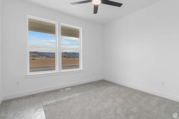 Empty room with a mountain view, light colored carpet, and a ceiling fan