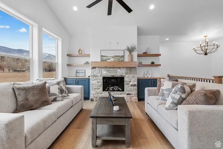 Living area featuring ceiling fan, light wood-type flooring, a fireplace, a chandelier, and a mountain view