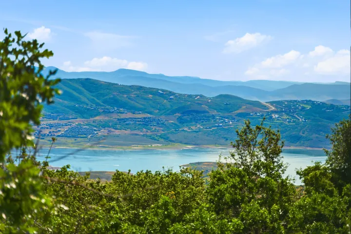 Expansive natural scenery featuring distant mountains, a prominent lake, and verdant foreground foliage