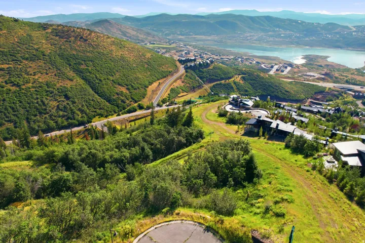 Hilly terrain with lush greenery, featuring a winding road and distant water body