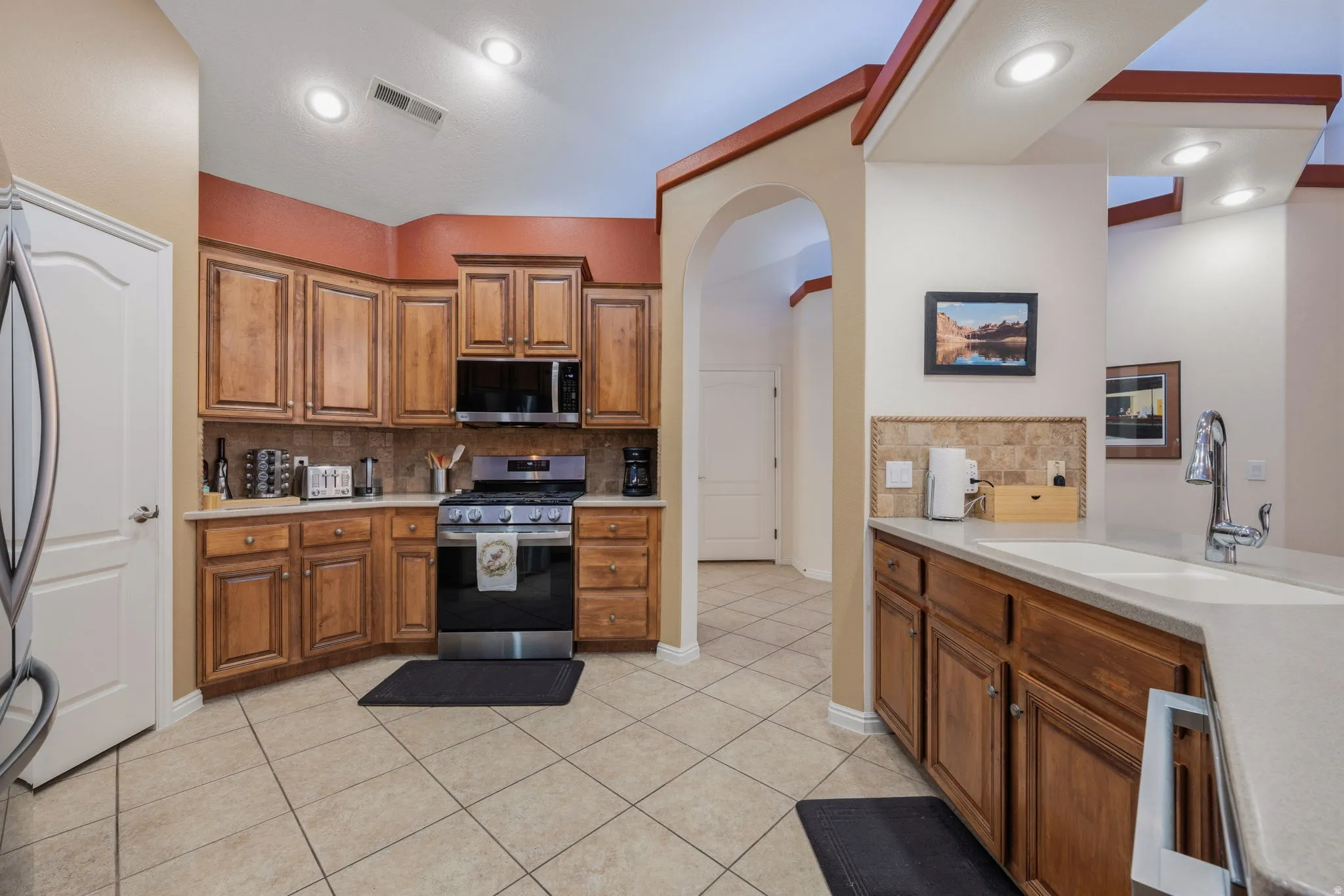 Kitchen with tasteful backsplash, arched walkways, wood finish cabinetry, stainless steel appliances, and light tile patterned floors