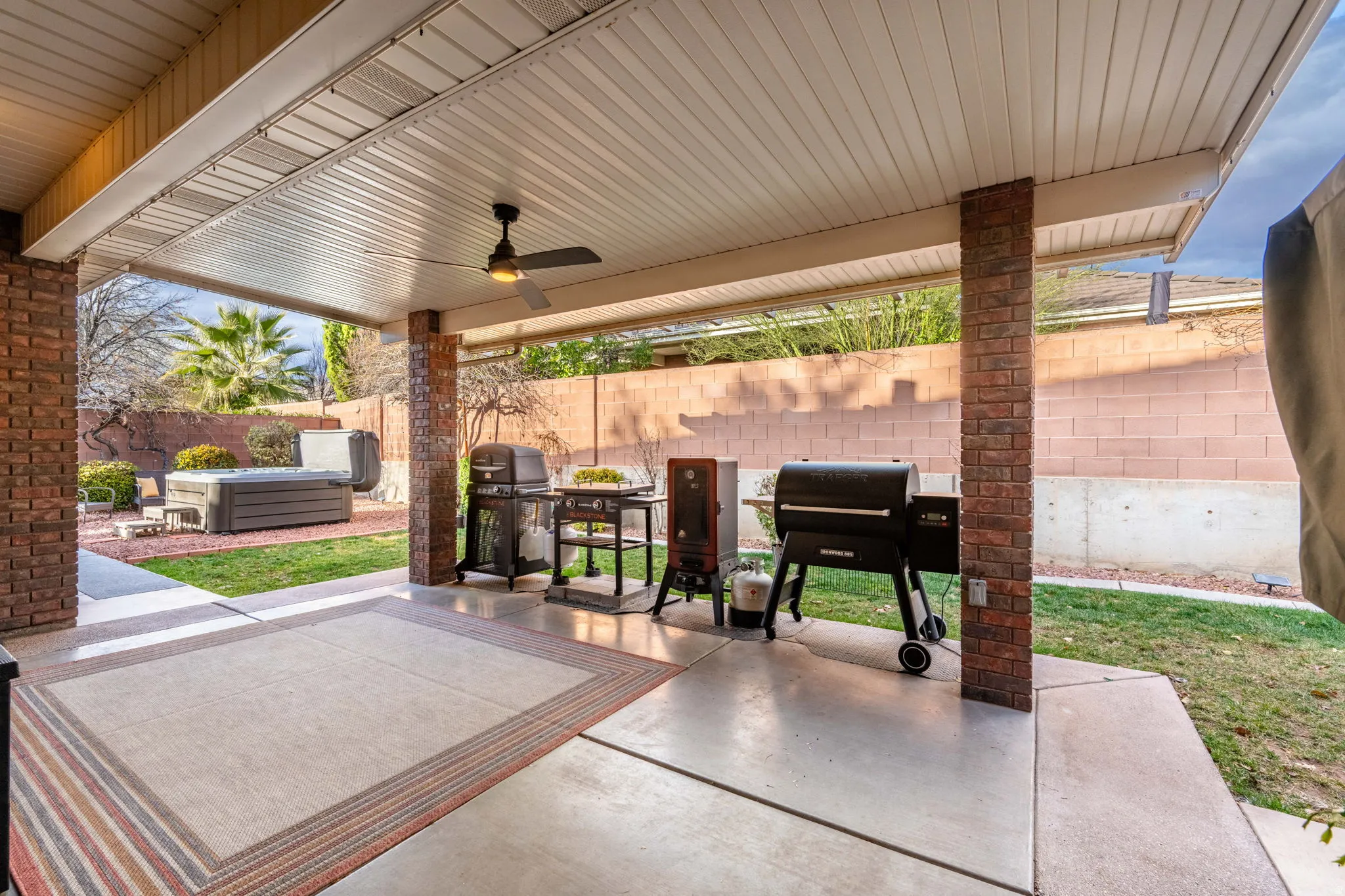 Fenced backyard with a patio, ceiling fan, grilling area, and a hot tub
